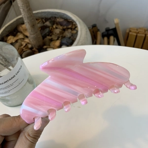 Pink and white striped acetate claw clip for hair styling in a warm lifestyle scene