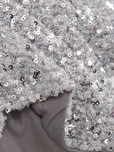 Dettaglio macro di paillettes argento su fodera in maglia grigia mostra la trama del tessuto