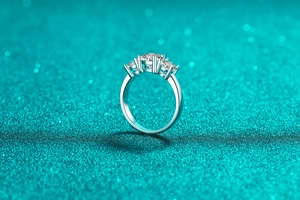 Detailed close-up of a three-stone moissanite ring on a shimmering teal glitter background