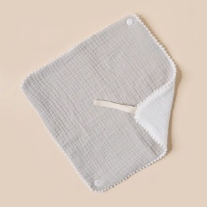 Detail of baby cotton gauze bib with white pom-pom trim and cotton hanging lanyard