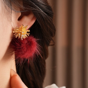 Close-up of elegant gold flower stud earrings with fluffy red pompom drops on model