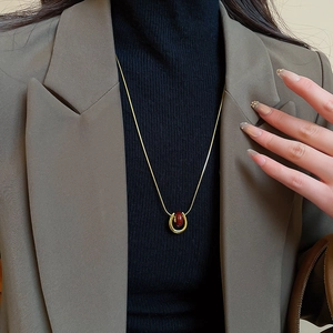 Detail of gold-plated U-shaped horseshoe pendant necklace with a deep red bead on a model