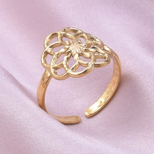 Détail macro d'une bague réglable en acier doré avec un motif de pétales ajourés