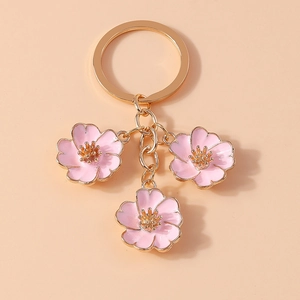 Detailed close-up of pink peach blossom charms with gold metal chain on a pink background
