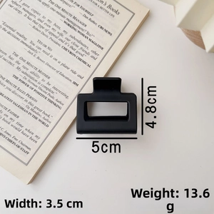Detail view of a matte black square hair claw clip on a book with size dimensions