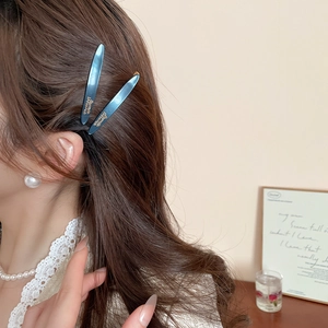 Dettaglio di due fermagli per capelli in resina blu scuro con scritte dorate su una modella