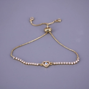 Detail of gold heart tennis bracelet with blue evil eye charm and adjustable toggle clasp