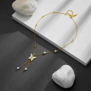 Detail of gold butterfly necklace with shell wings, green gem, and pearl tassels