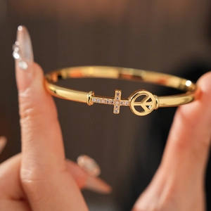 Detail of gold-plated bracelet with cross and peace sign featuring zircon stones