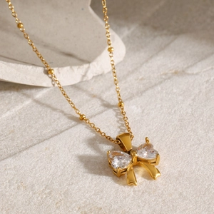 Close-up of 18k gold plated bow pendant with heart-shaped white zircon and beaded chain