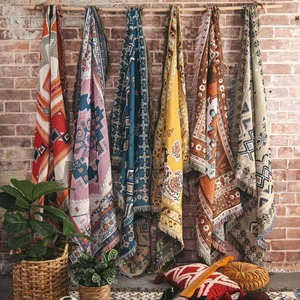 Close-up of bohemian woven blankets with geometric patterns and fringe detail on brick wall