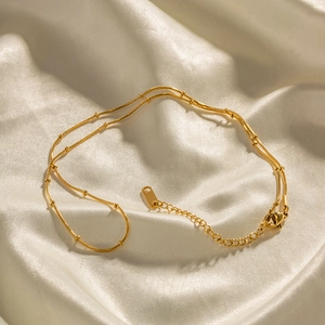 Macro shot of gold ball chain necklace with lobster clasp on white silk fabric