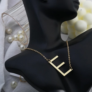 Detailed view of elegant gold letter E pendant necklace on black mannequin