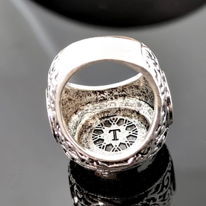 Gros plan sur une bague argentée vintage avec relief et gravure de la lettre T à l'intérieur