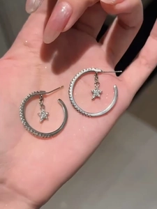 Detail of silver C-shape hoop earrings with sparkling zircon star pendants held in hand