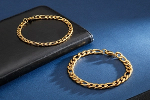 Detailed close-up of golden Figaro chain bracelets on black leather and blue matte surface