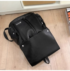 Dettaglio zaino in pelle nera con patta, fibbia metallica e logo SUNMAN su fondo legno