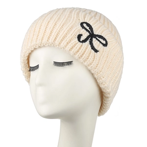 Détail du bonnet en maille blanc crème avec broderie de nœud noir et texture côtelée