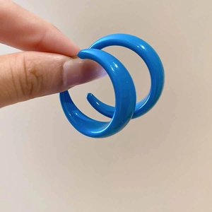 Close-up of bright blue acrylic C-shaped crescent earrings held for detail view