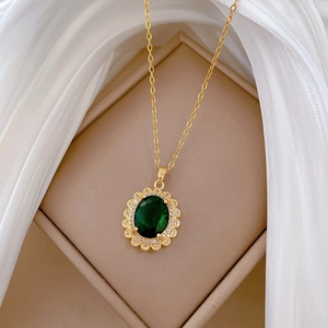 Dettaglio di una collana vintage dorata con pendente ovale verde su seta bianca