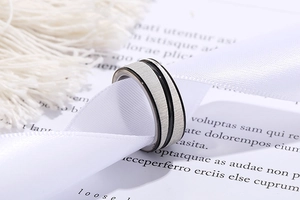 Macro detail of silver brushed stainless steel ring with parallel black lines on silk