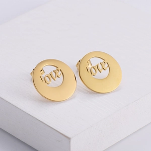 Golden titanium steel hoop earrings featuring hollowed love letter design on white pedestals