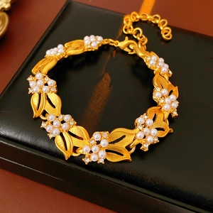 Close-up of a gold leaf bracelet with white pearls and sparkling zircons on a leather surface