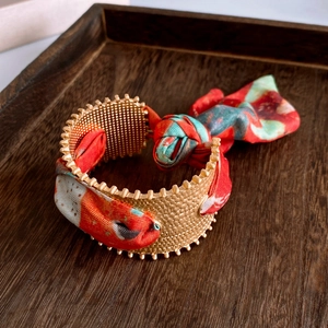 Detail view of a gold textured cuff bracelet featuring a stylish red and green silk scarf wrap