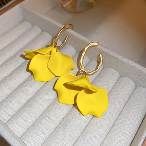 Macro detail of yellow petal earrings with gold textured C-shape hoops on velvet