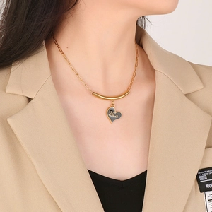 Golden heart pendant necklace with black enamel center and Love engraving on a model