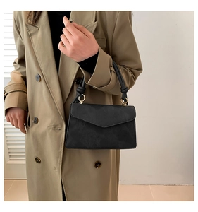 Détail du sac noir avec poignée à nœud, rabat en V et finitions métalliques dorées