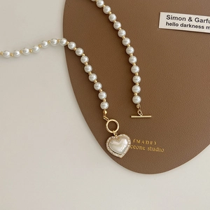 Detail of a pearl heart pendant necklace featuring a gold toggle clasp and sparkling zircons