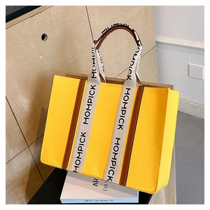 Detail of yellow felt tote bag featuring contrast leather trim and lettered handles