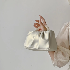 Detail view of the white pleated cloud bag featuring a luxury pearl handle and soft leather