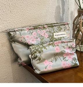 Set of two satin makeup bags in grey-green and pink floral patterns on a wooden table