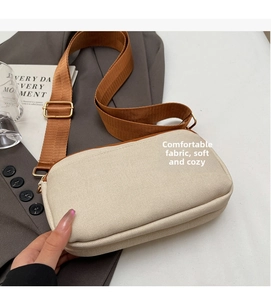 Detail of off-white canvas crossbody bag with brown strap and gold metal buckle adjusters