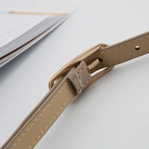 Macro shot of beige leather belt featuring fine stitching and a polished gold pin buckle