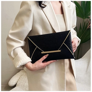 Détail d'une pochette enveloppe noire scintillante avec finitions dorées portée par un mannequin