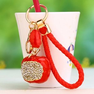 Detailed close-up of a red rhinestone apple keychain hanging on a white cup rim