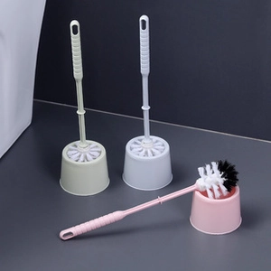 Three colorful plastic toilet brush sets in green, white, and pink on a grey surface