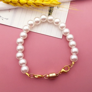 Detail of white pearl bracelet with a golden magnetic clasp on a soft pink background