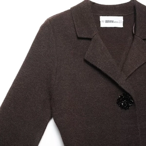 Close-up of knit blazer showing notched lapel and black floral jewelry button detail