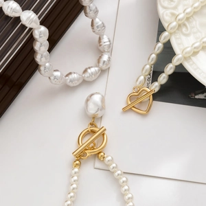 Detail of layered baroque pearl necklaces with golden heart-shaped toggle clasps on a plate