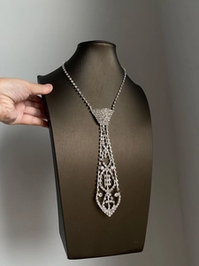 Macro shot of a silver rhinestone-studded necktie necklace on a black display stand