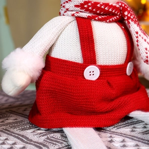 Détails du tricot d'une poupée de Noël avec jupe à bretelles rouge et boutons blancs