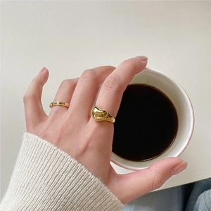 Close-up of golden vintage heart embossed ring and thin band on model holding a coffee cup