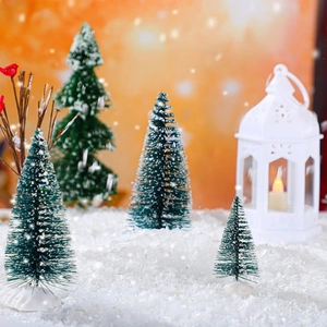 Miniature green Christmas trees and white glowing lantern in artificial snow scenery