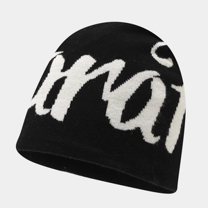 Detail showing the white jacquard letter knit texture on a black street style beanie