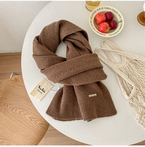 Detail of 100% pure wool scarf texture with brand metal tag on a minimal desk