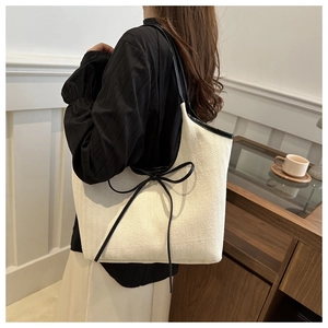 Detail of canvas tote bag featuring contrast black leather bow and textured fabric finish